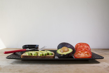 Avocado toast with sliced tomatoes and green onions on multigrain toast. Served on a wooden platform.