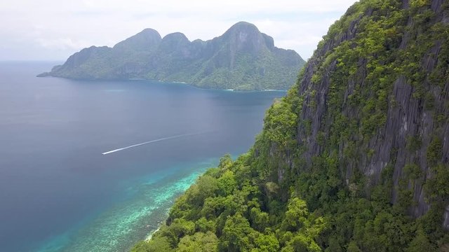 Aerial drone view of towering jungle covered cliffs and tropical coral reef below