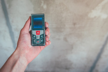 Hand holding construction roulette, calliper and laser range finder on wall background. Laser measuring tool.