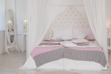Fototapeta na wymiar Big bed with cute pastel bedding in woman's room. Modern bedroom in pastel colors. four-poster bed.Scandinavian simplicity design. Eco loft apartments.