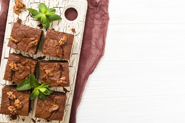 Brownie sweet chocolate dessert with walnuts and meant leaves on retro board with copy space on pastel beige background.