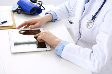 Woman doctor using tablet computer while sitting at the desk in hospital closeup. Cardiologist checks heart diagrams with tablet pc. Healthcare, insurance and smart technology in medicine concept