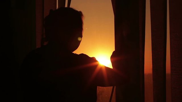 Silhouette of a woman looking out the window at sunset