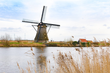 Naklejka premium Traditional Dutch windmills near the water canals with beautiful white clouds and blue sky reflecting in water. UNESCO world heritage sight in Kinderdijk, Netherlands in winter