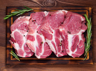 Raw Pork Loin chops on a cutting board with herbs rosemary on dark wooden background, top view