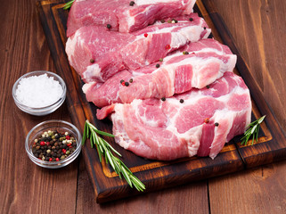 Raw Pork Loin chops on a cutting board with herbs rosemary on dark wooden background, side view