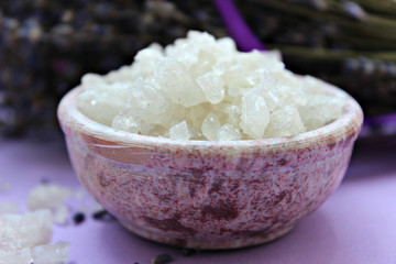 Large crystals of sea salt and lavender flowers, close-up on a purple background. Aromatherapy and Spa treatments, bathing, relaxation
