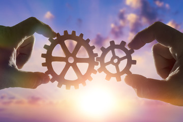 two hands connect the gears, the details of the puzzle. against the sky with sunset. Business concept idea, cooperation strategy, teamwork, innovation, creativity