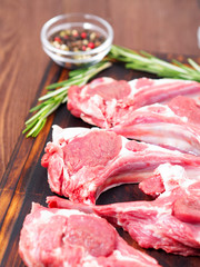 Raw lamb cutlets on bone on dark brown wooden background, lamb ribs, side view, vertical