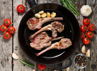 Roasted lamb ribs with rosemary, tomatoes and garlic on pan on dark old rustic wooden background, top view