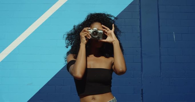 Beautiful young woman shooting photos with film camera against colorful blue wall