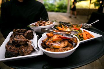 Dinner food including steak, fish, fruit, and vegetables being held by a banquet server