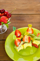 canapé of peaches, kiwi and strawberries on a white plate. next to the pial of strawberries and cherries. vertical photo.