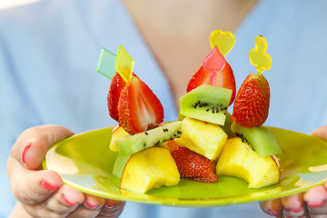 a plate of canapé of kiwi, strawberries and peaches in the hands of a woman. close-up. horizontal photo.