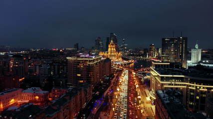 Fototapeta premium Bright lights of night Moscow from bird's eye view. Intensive traffic at New Arbat street in the heart of the city. Multistory houses illuminated with neon lights on the sides of the wide avenue.