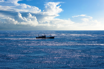 Fishing boat in open sea with amazing cloudscape in background