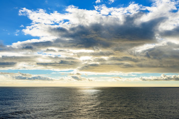 Fototapeta na wymiar Dramatic golden sunset at open sea: sun rays shining through dark clouds