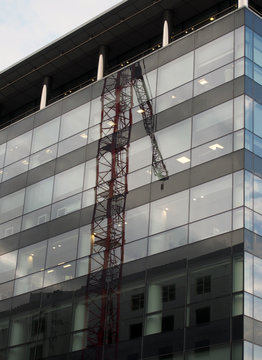 the corner of a modern glass and black office building with reflection of a construction crane on the windows and blue sky