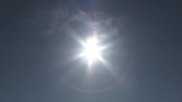 From wide shot, camera zoom into bright sun on clear day causing warp effect and solar flares transition to white frame.