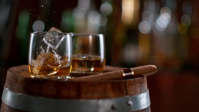 Ice dropped into glass of whisky on barrel in super slow motion. Shot with high speed cinema camera Phantom VEO 4K , 1000fps.