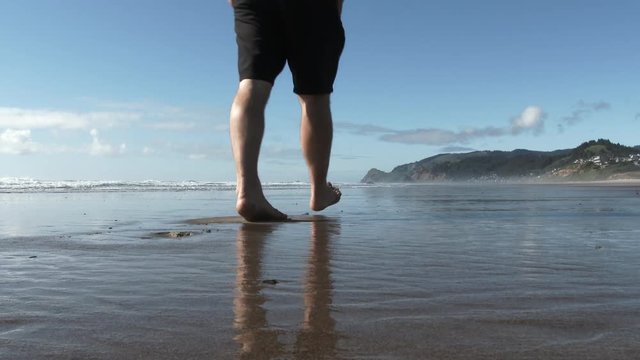 Model released person walks down sandy beach on sunny day at the Oregon Coast, low and wide angle.