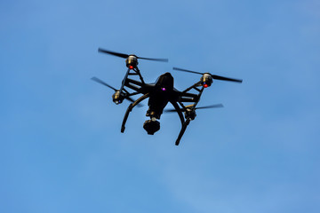 Black drone quadcopter with camera flying over blue sky. Angle view