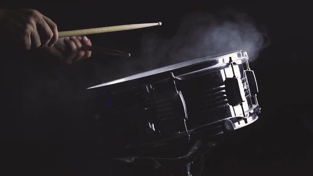 Dust from snare drum with hand and drum sticks in black background, close-up, low key, video, footage, cinemagraph style.