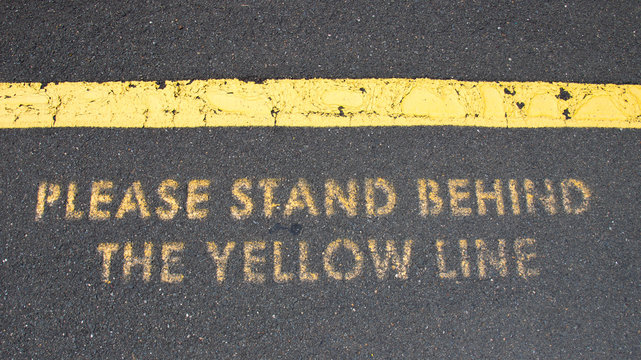 駅のプラットフォームで、"PLESE STAND BEHIND THE YELLOW LINE&rdquo;
