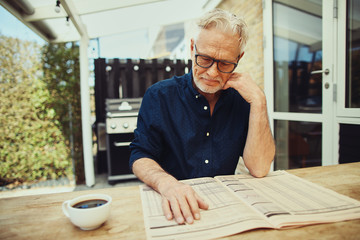 Senior man sitting outside drinking coffee and reading a newspap