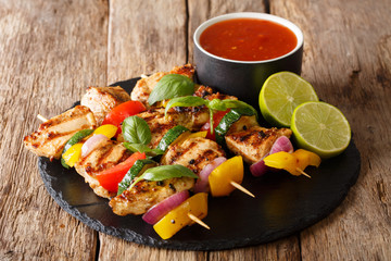 Organic grilled chicken kebab skewers with vegetables served with sauce, herbs and lime closeup on a slate plate. horizontal