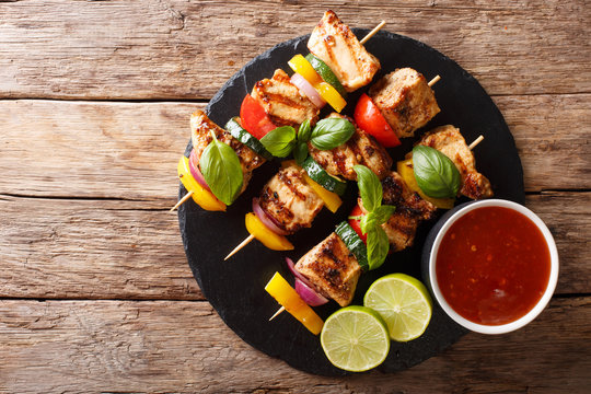 Hot grilled chicken kebab skewers with colorful vegetables with sauce, basil and lime closeup. horizontal top view