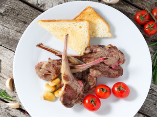 fried lamb ribs with tomatoes on white plate on a gray old wooden table, top view