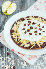 Homemade chocolate oat pancakes with apple, yogurt, cottage cheese, raisin and flowers on grey wooden background. Healthy breakfast or snack.