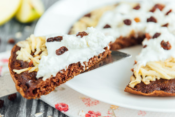 Homemade chocolate oat pancakes with apple, yogurt, cottage cheese, raisin and flowers on grey wooden background. Healthy breakfast or snack.