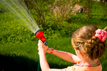 Little child, adorable toddler girl, watering the plants, green lawn, from hose spray in the garden...