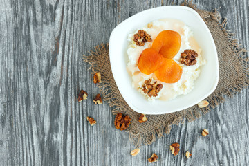 Cottage cheese with sour cream, dried apricot and walnut on grey wooden background.