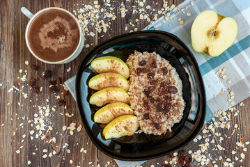 Oatmeal with apple, cinnamon, raisin and flax seeds on black plate on dark wooden background. Healthy breakfast.