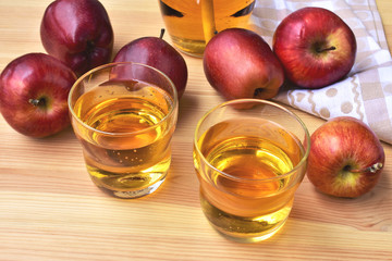 Apple juice in a two glasses, whole red apples on a wooden table.
