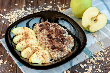 Oatmeal with apple, cinnamon, raisin and flax seeds on black plate on dark wooden background. Healthy breakfast.