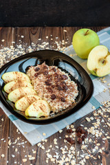 Oatmeal with apple, cinnamon, raisin and flax seeds on black plate on dark wooden background. Healthy breakfast.
