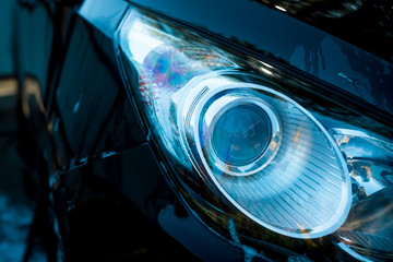 Car headlight with shallow depth of field. Luxury Cars Headlight, exterior details. Black car in washing process. Copy space