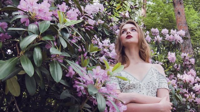 Beautiful young woman in flowers. Girl in beautiful elegant summer long dress posing on background of flowers inspiration. Young lovely woman in spring flowers. Girl stands among the flowering trees.