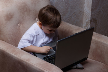 the boy is sitting on a chair and is holding a laptop