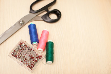 Fototapeta na wymiar On the cutting table lie scissors, thread and pins. Work place of seamstress. topp view, place for text