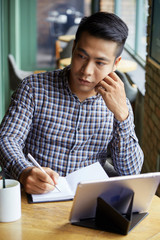 Young man writing plans in notebook while sitting at cafe