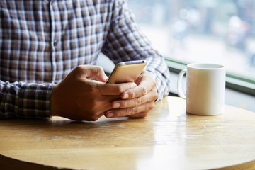 Close-up of man sitting at the table at cafe and typing on his smartphone