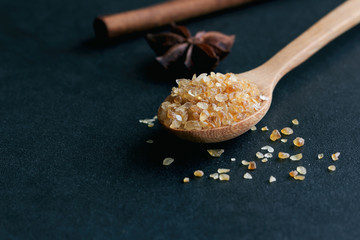 Natural brown sugar or no bleach sugar on wood spoon and cinnamon stick and anise on black granite table with copy space. Sweet seasoning for good health. Ingredient prepared for cooking or bakery.