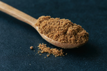 Natural brown sugar or unrefined sugar on wood spoon on black granite table in close up view macro...