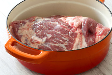 Raw shoulder of lamb in an orange ceramic roasting dish prepared to be cooked