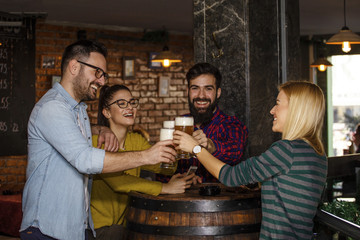 Group of four people toasting with glasses full of beer in local pub